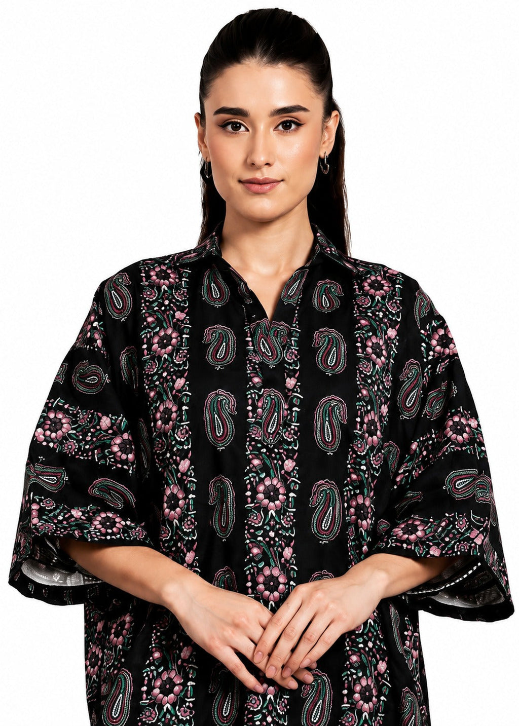 A woman modeling a black kaftan-style top with pink, green, and white paisley and floral patterns, set against a plain white background.