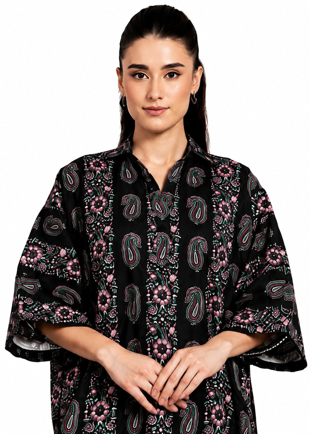 A woman modeling a black kaftan-style top with pink, green, and white paisley and floral patterns, set against a plain white background.