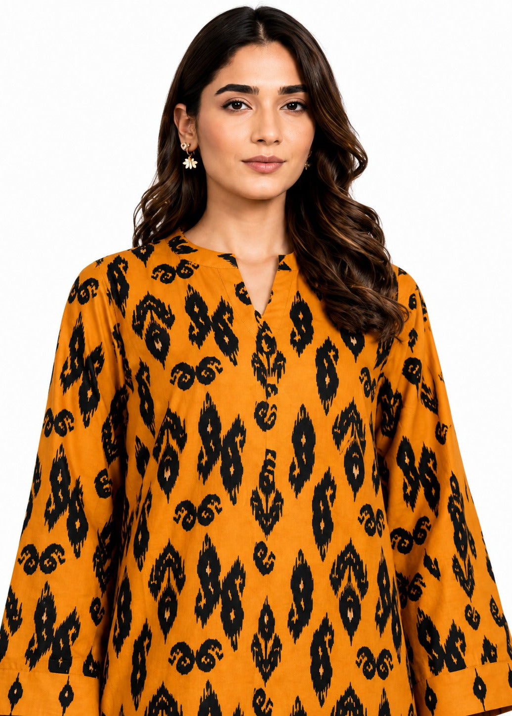 A woman wearing a mustard yellow long-sleeve tunic top with a black ikat pattern, photographed against a solid white background.