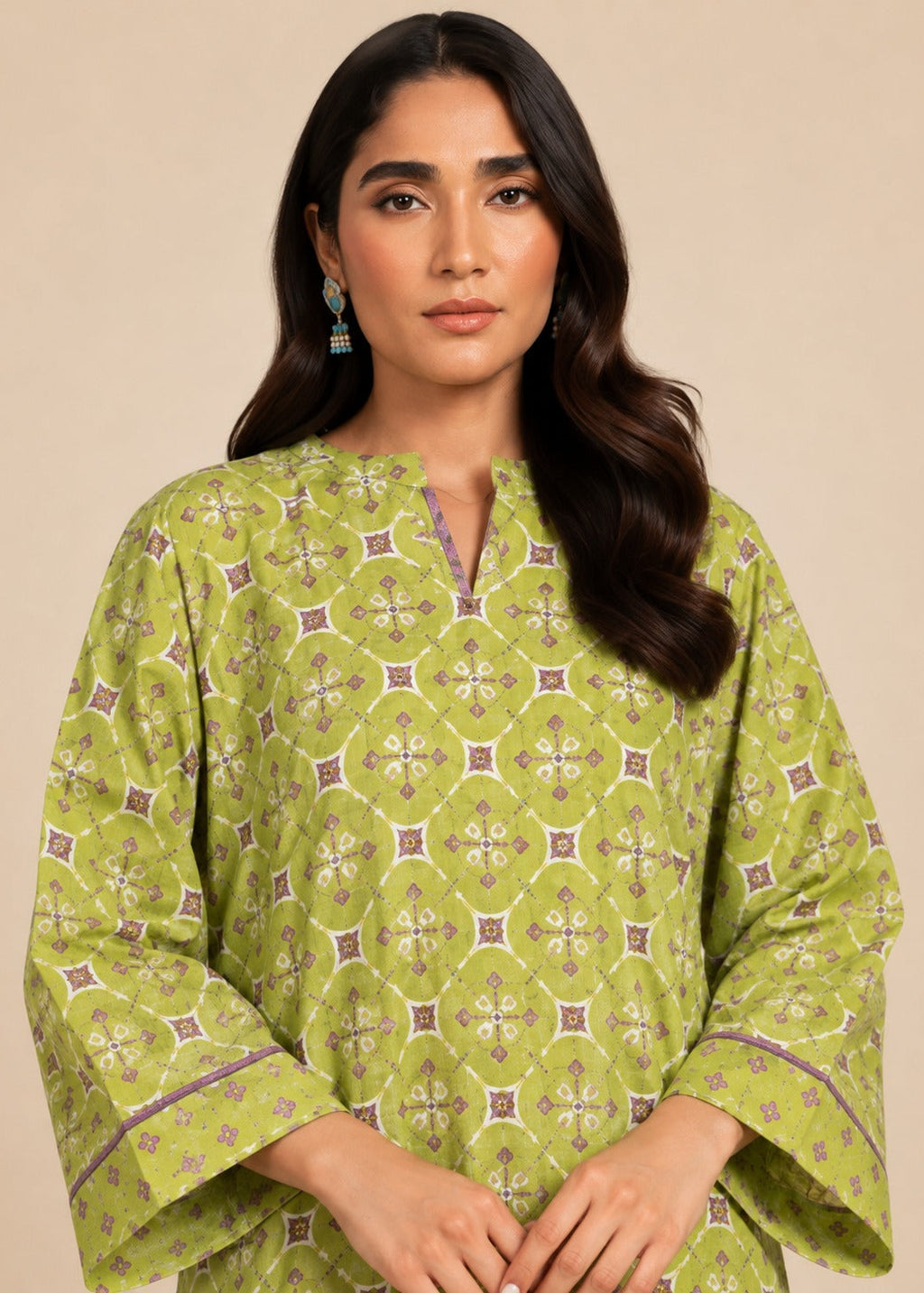 A woman wearing a light olive green kurta with a detailed geometric block print pattern in beige, brown, and purple, set against a solid beige background.