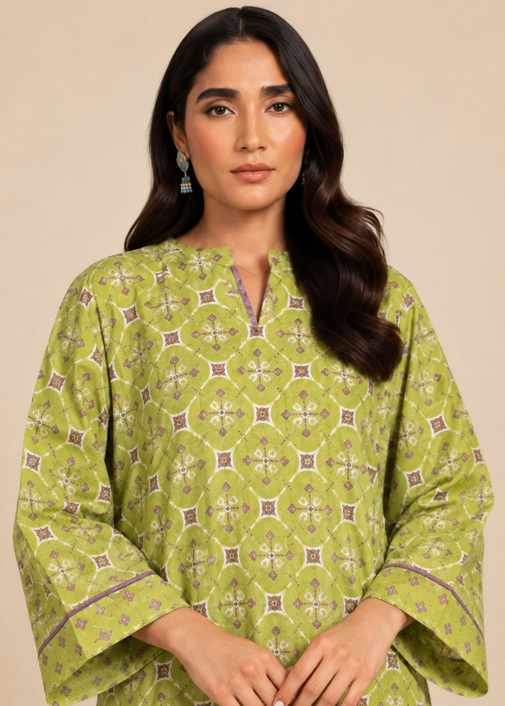 A woman wearing a light olive green kurta with a detailed geometric block print pattern in beige, brown, and purple, set against a solid beige background.