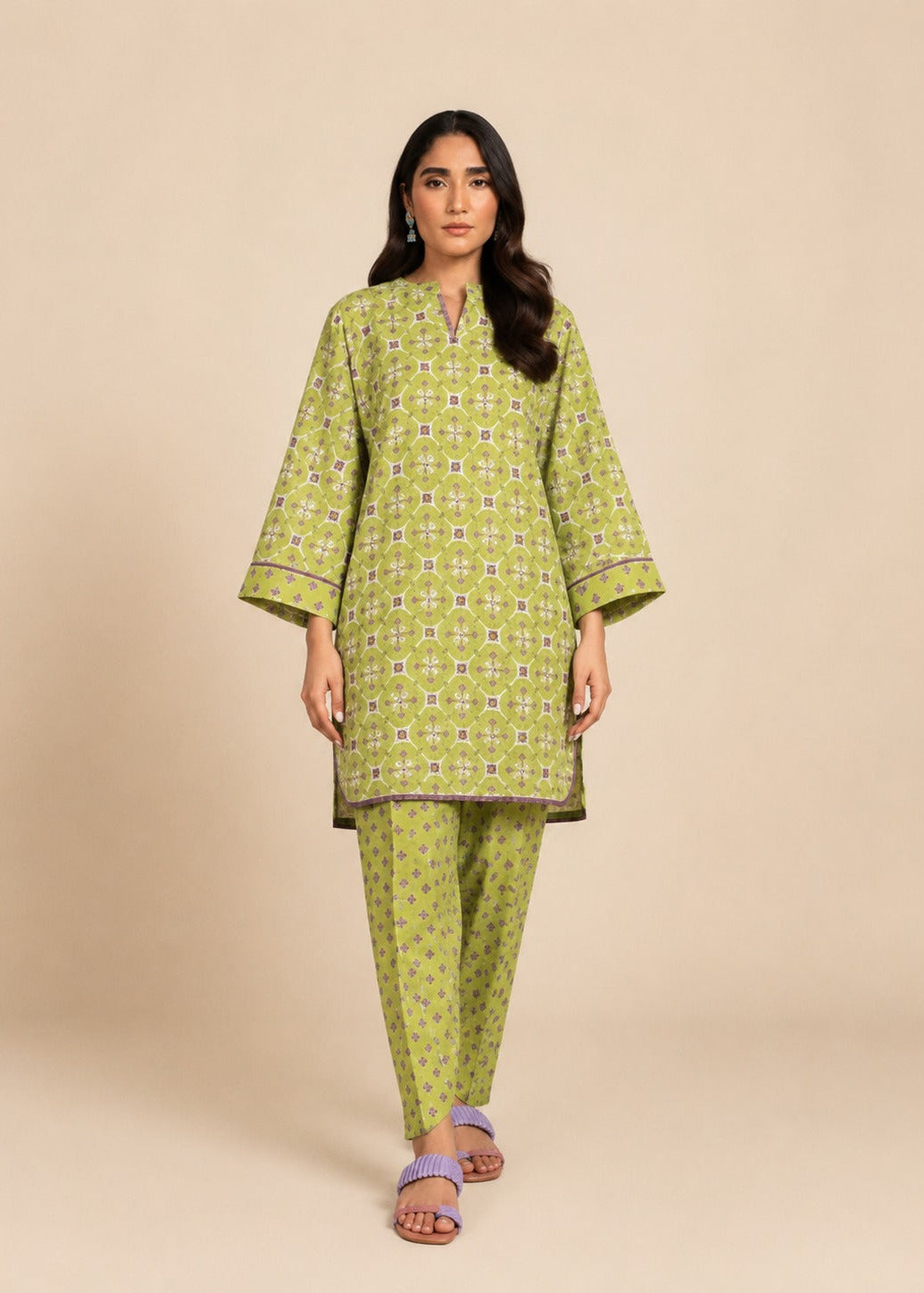 A woman modeling a light green kurta and matching pants set with a white geometric pattern, photographed against a solid beige studio background.