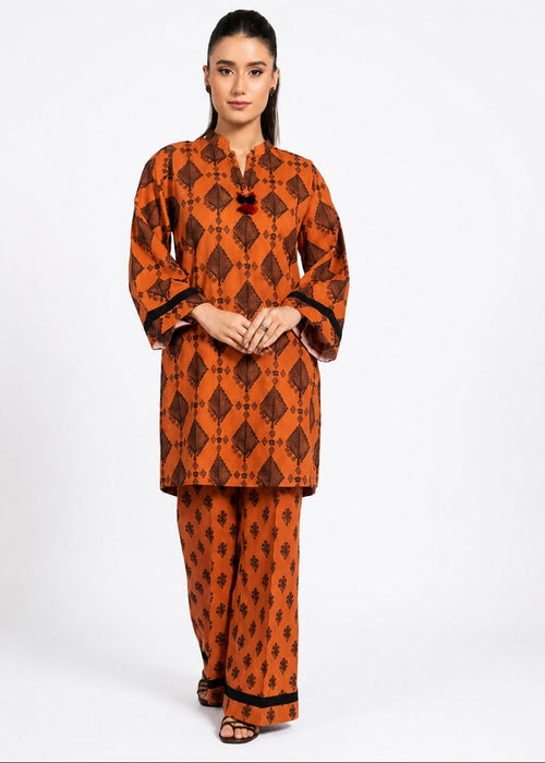 A woman modeling a matching orange and black printed kurta and trouser set against a plain white studio background.