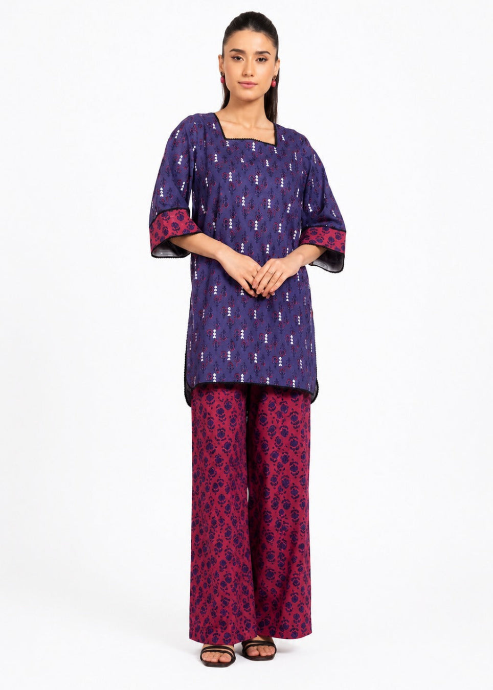 A woman modeling a two-piece traditional outfit consisting of a purple kurta with small white motifs and pink patterned cuffs, paired with matching wide-leg trousers in purple and pink, shot against a plain white background.