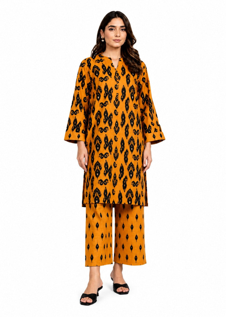 A woman modeling a matching two-piece kurta and trouser set in mustard yellow with a black ikat pattern, photographed against a solid white background.