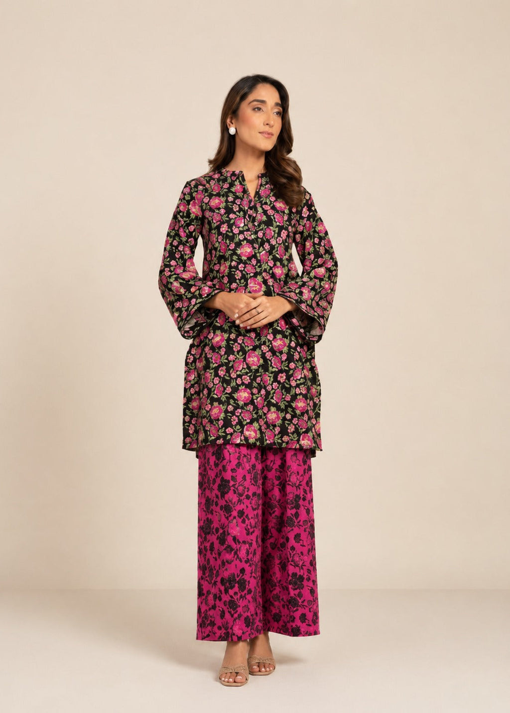 A woman modeling a two-piece floral printed outfit consisting of a black long-sleeve kurta with pink and green floral patterns and matching wide-leg trousers in bright pink and black.