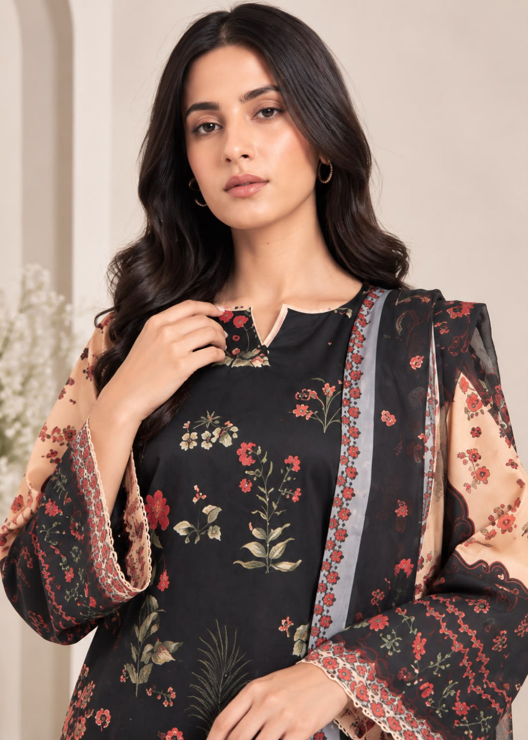A woman modeling a black floral printed kurta with matching sheer sleeves and a sheer dupatta featuring red and beige floral patterns, set against a soft beige background.