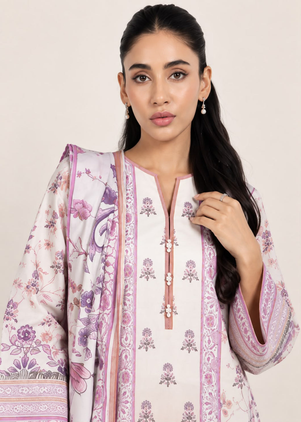 A woman modeling a traditional South Asian outfit featuring a white kurta with purple floral prints and borders, paired with a matching patterned dupatta, set against a solid light beige background.
