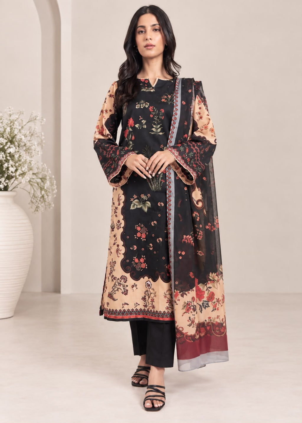 A woman modeling a traditional three-piece salwar kameez suit set. The set features a black long kurta with beige floral borders, black trousers, and a matching black dupatta with beige floral prints and a gray border.