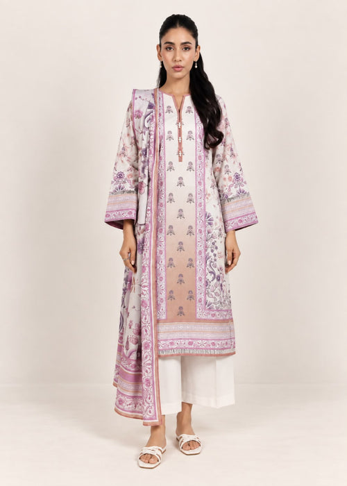 A woman modeling a traditional South Asian outfit featuring a long beige kurta with pink and purple floral prints, white pants, and white slide sandals, set against a plain light beige studio background.