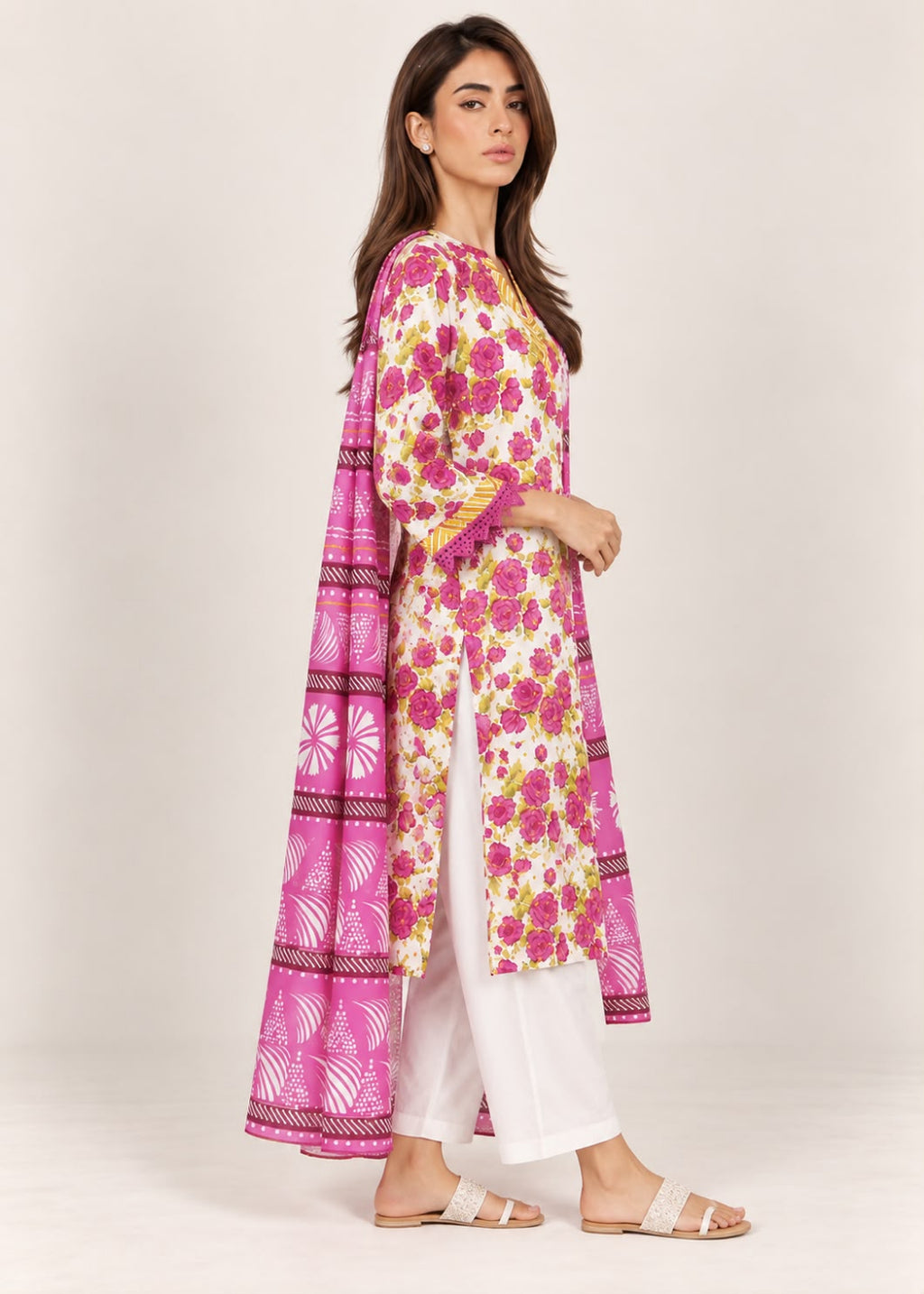 A woman modeling a long pink and white printed kurta with white pants and flat sandals, standing against a plain light beige studio background.