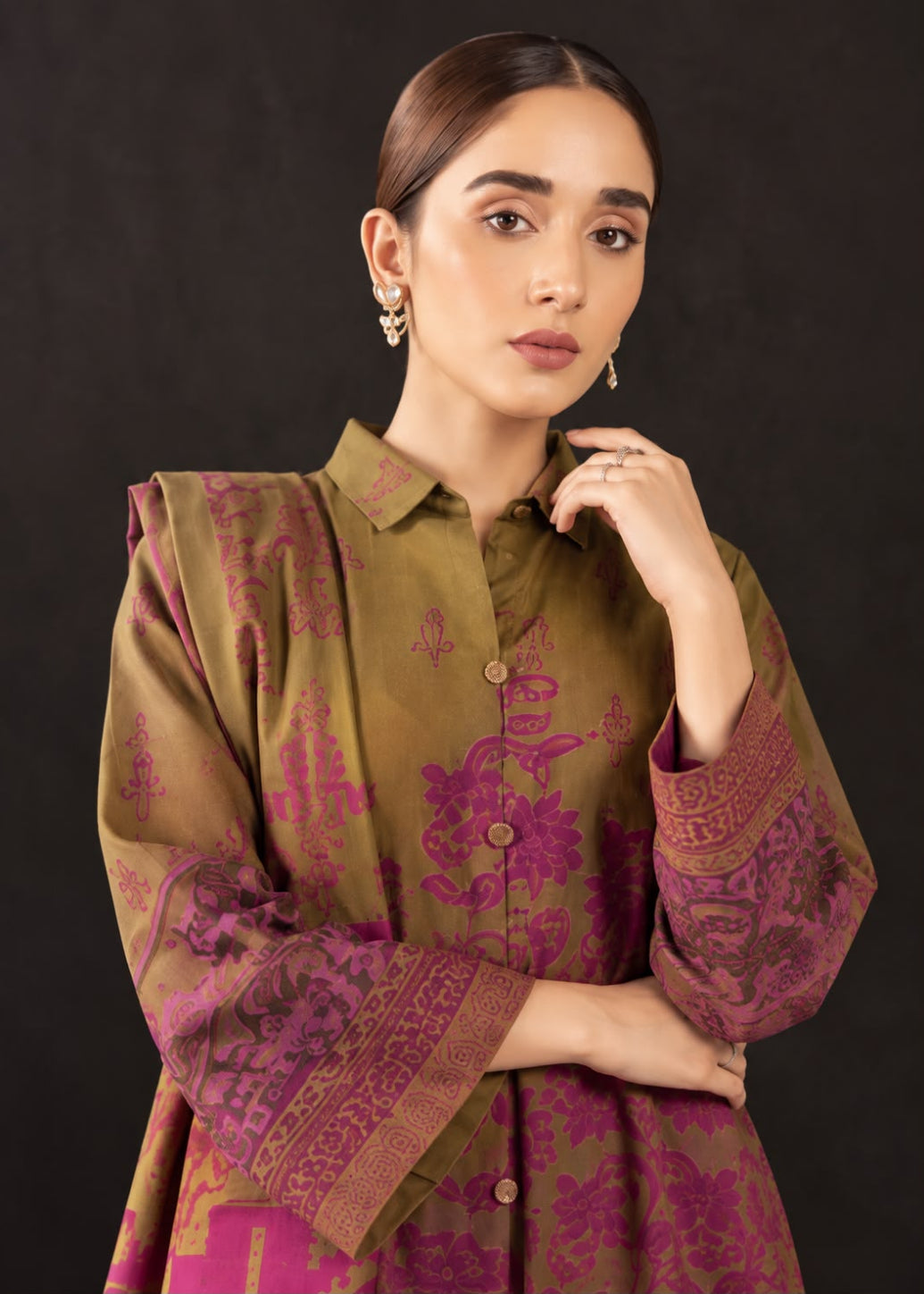 A woman modeling a traditional button-up kurta in olive green and magenta with intricate floral and border patterns, set against a dark studio background.