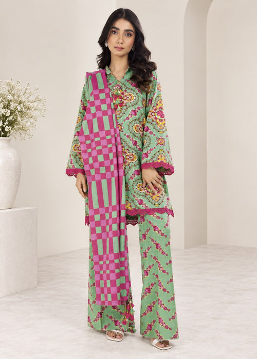 A woman modeling a three-piece green and pink traditional outfit with floral prints, checkered patterns, and wide-leg pants, standing in a minimalist beige room.