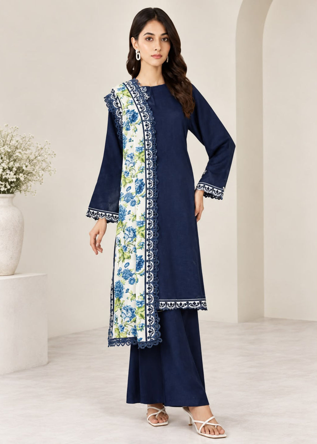 A woman models a navy blue three-piece salwar kameez set with a white dupatta featuring blue and green floral patterns and a blue border. The set includes a long-sleeved kameez top, matching navy pants, and a coordinating navy dupatta.