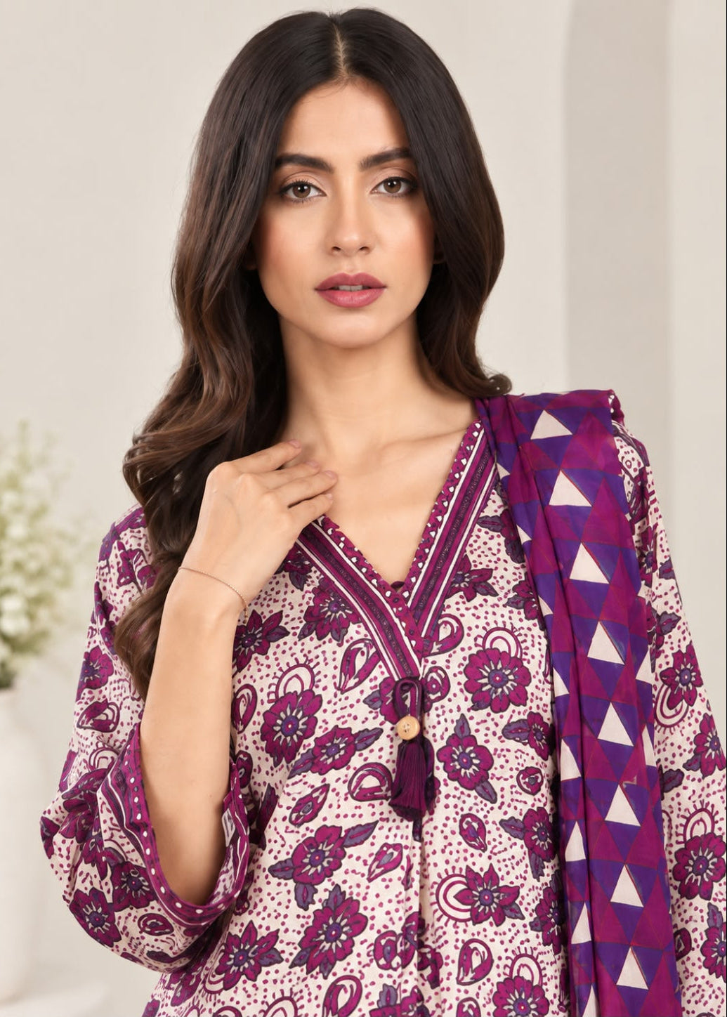 A woman modeling a traditional Indian salwar kameez set featuring a purple and pink paisley print with a matching patterned dupatta.