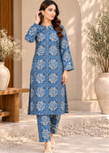 A woman models a blue three-piece kurta set with white geometric patterns, consisting of a long tunic, matching pants, and a folded top, set against a warm, sunlit architectural background.