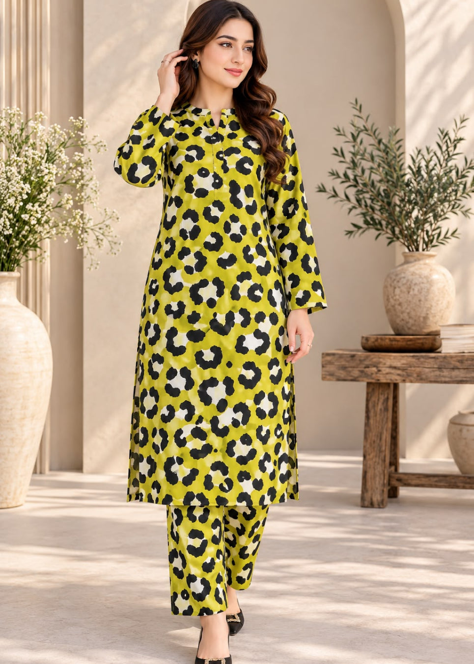 A woman models a bright yellow-green kurta set with a black and white leopard print pattern, styled with matching pants and black flat shoes in an elegant indoor setting with plants.