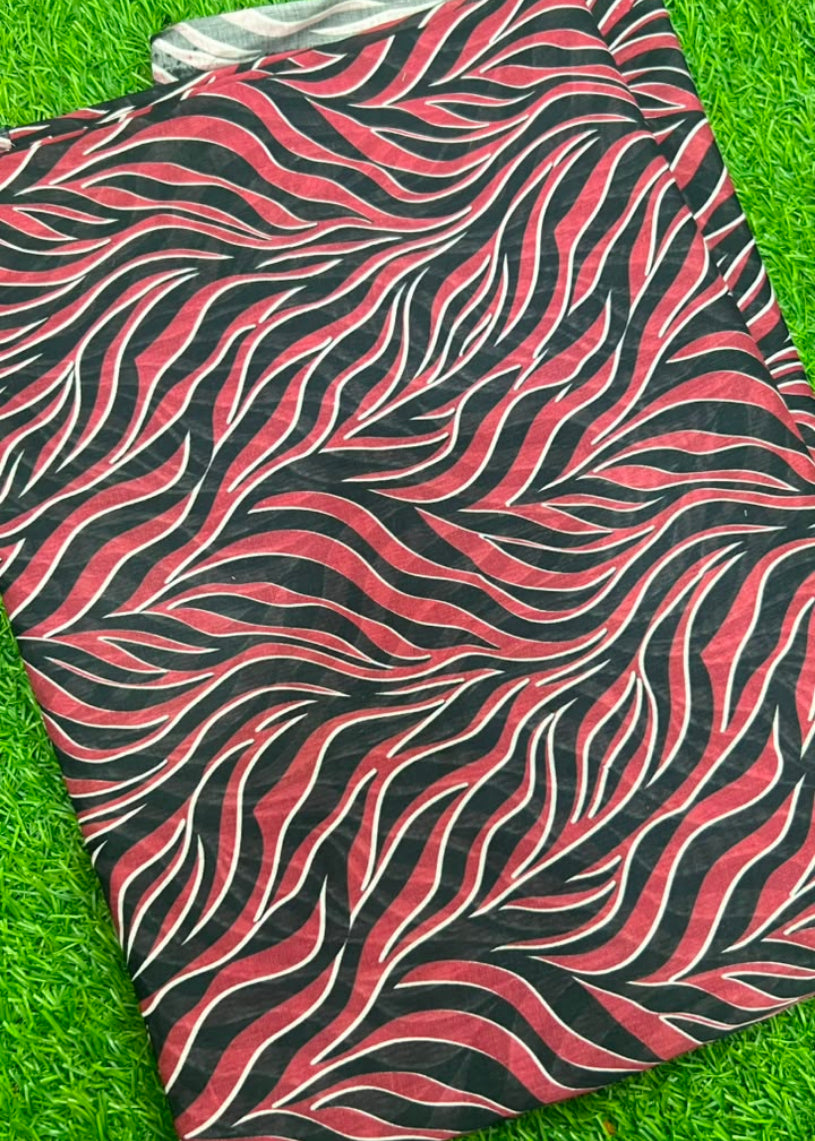 A folded fabric item, likely a scarf or shawl, featuring a bold wavy zebra-like pattern in black, red, and white, laid flat on a bright green grass background.