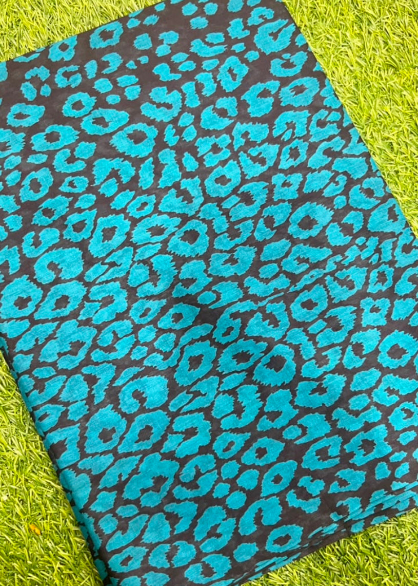 A folded piece of fabric with a vibrant turquoise blue leopard print on a black background, laid flat on a bright green grass-like surface.