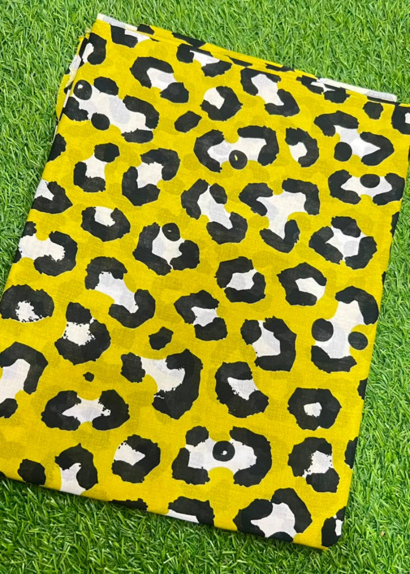 A folded piece of fabric with a bold yellow, black, and white leopard print pattern, laid flat on a green grass background.
