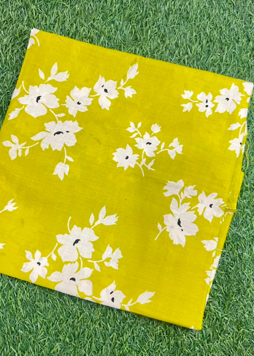 A folded yellow fabric item, likely a scarf or bandana, featuring a white floral pattern, laid flat on green grass.