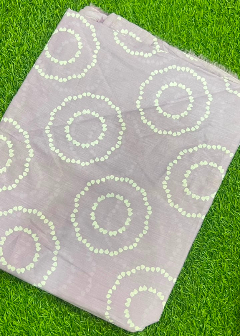 A folded light purple fabric with white circular dot patterns, laid flat on a green grass background.