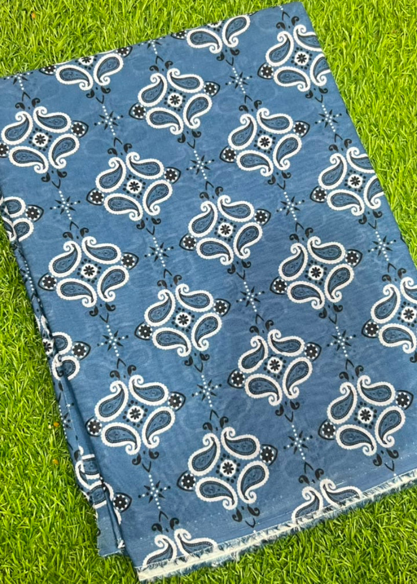 A folded piece of blue fabric with a white and black paisley block print pattern, laid flat on a green grass background.
