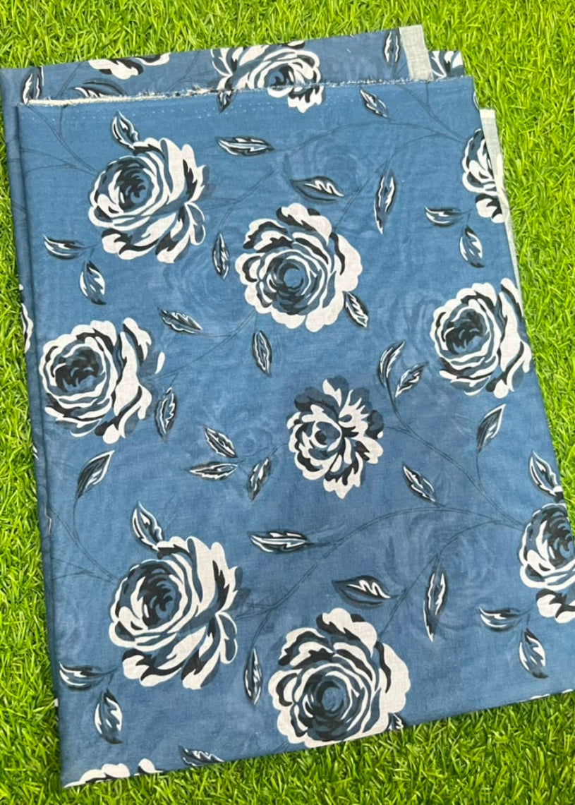A folded piece of blue fabric with a white and gray floral rose pattern, laid flat on a green grass background.