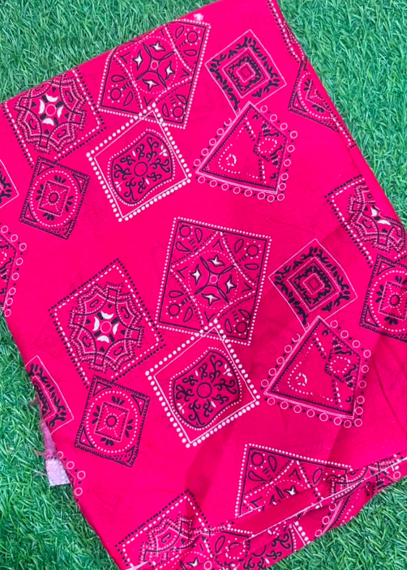 Bright pink fabric with black and white geometric bandhani-style patterns, laid flat on green artificial grass.