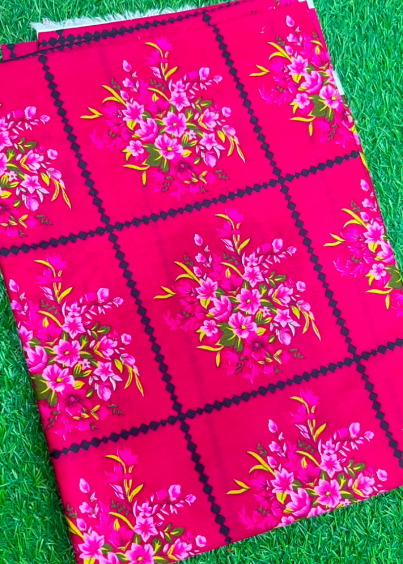 A folded piece of bright pink fabric with a black grid pattern and pink floral motifs, laid flat on a green grass-like surface.
