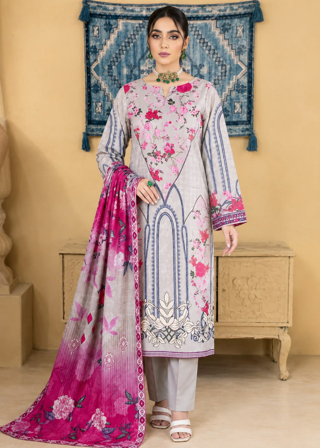 A woman models a traditional South Asian salwar kameez suit set. The set features a light gray kameez jacket with pink and blue floral embroidery, matching gray trousers, and a vibrant pink dupatta with blue and white floral patterns.