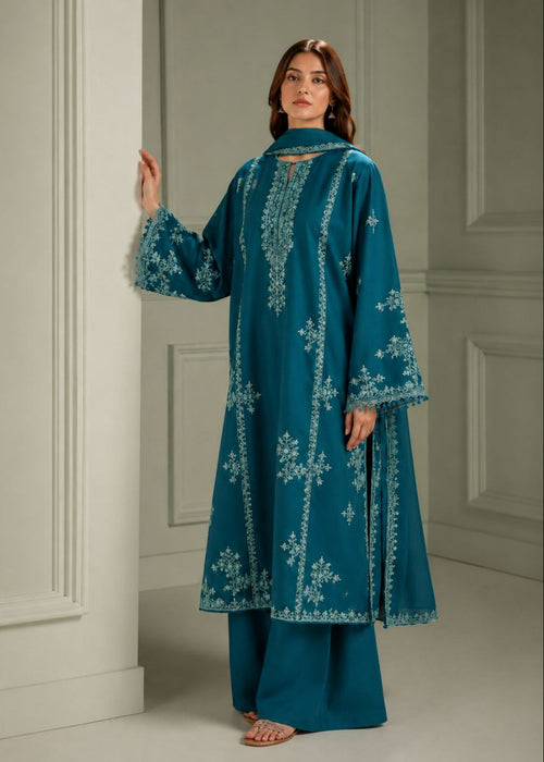 A woman models a teal blue embroidered kurta and matching wide-leg trousers in an elegant indoor setting with white paneled walls.