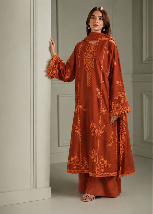 A woman models a rust-orange embroidered kurta and matching trousers with a coordinating dupatta in a classic interior setting.