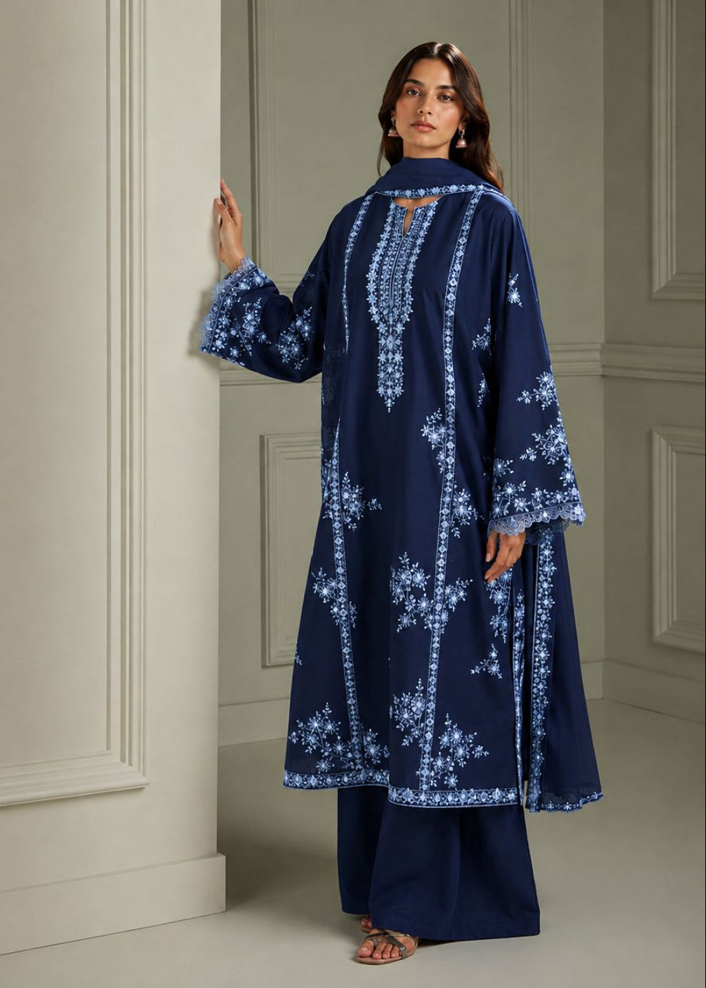 A woman models a navy blue long kurta with intricate white floral embroidery, paired with matching navy wide-leg trousers, set against a classic cream-colored paneled wall.