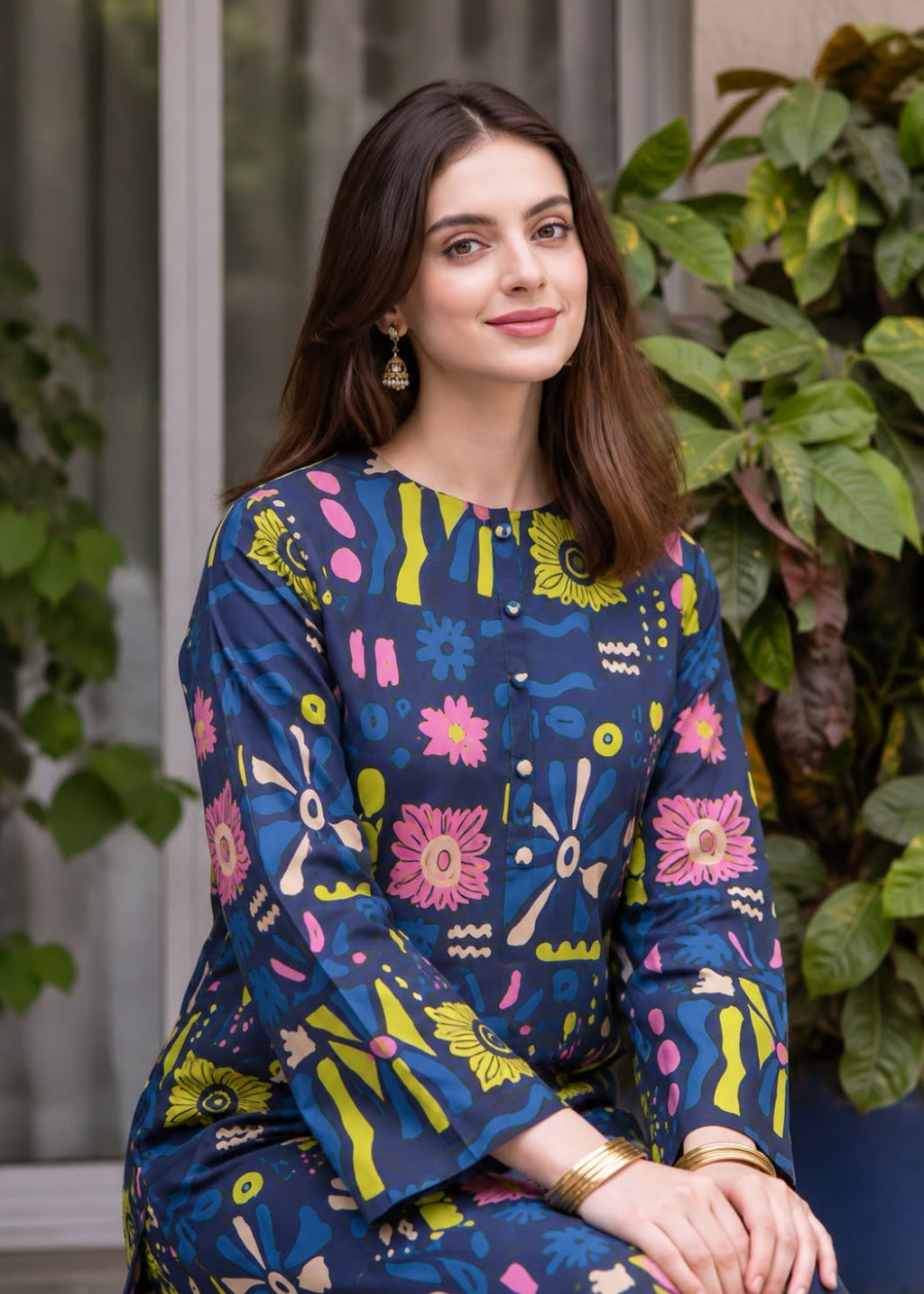 A woman wearing a navy blue long-sleeve kurta with a colorful abstract floral print in pink, yellow, and green, posed in front of a window and green plants.