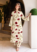 A woman models a cream-colored long-sleeve kurta and matching pants set with a red rose and green leaf floral pattern, standing in an indoor setting with a staircase and potted plants.