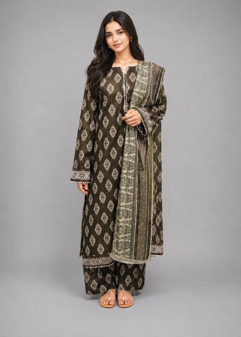 A woman modeling a traditional three-piece salwar kameez suit in dark brown and olive green with intricate silver embroidery, paired with matching trousers and a dupatta, set against a solid gray studio background.