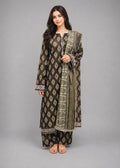 A woman modeling a traditional three-piece salwar kameez suit in dark brown and olive green with intricate silver embroidery, paired with matching trousers and a dupatta, set against a solid gray studio background.