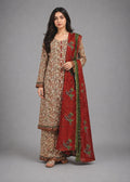 A woman modeling a traditional South Asian salwar kameez set. The outfit features a beige and brown floral-patterned kurta and matching trousers, paired with a deep red dupatta decorated with green borders and floral embroidery.