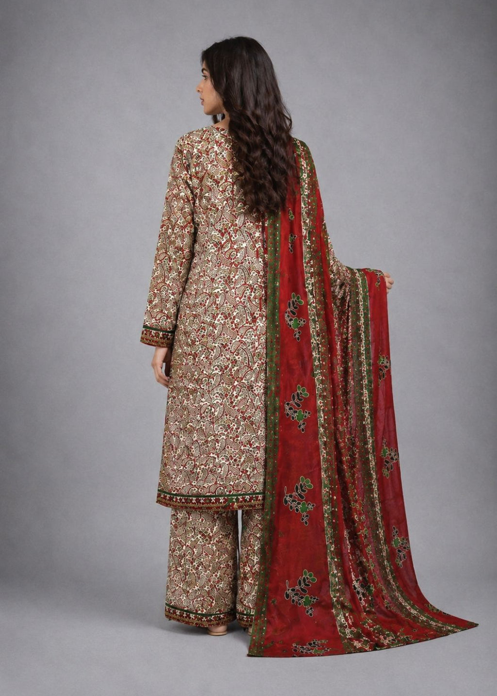 A woman modeling a traditional three-piece salwar kameez suit in a studio setting. The outfit features an intricate beige and gold floral embroidered kurta and matching trousers, paired with a vibrant red dupatta decorated with gold and green floral patterns.