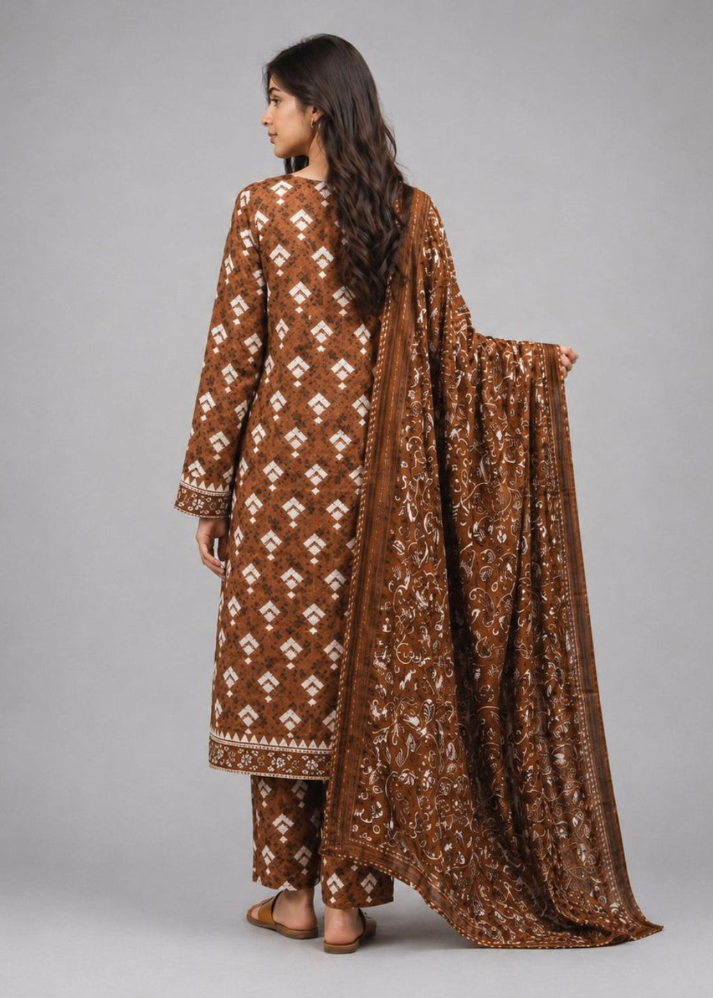 A woman modeling a brown traditional outfit with white geometric patterns, shown from the back against a solid gray studio background.