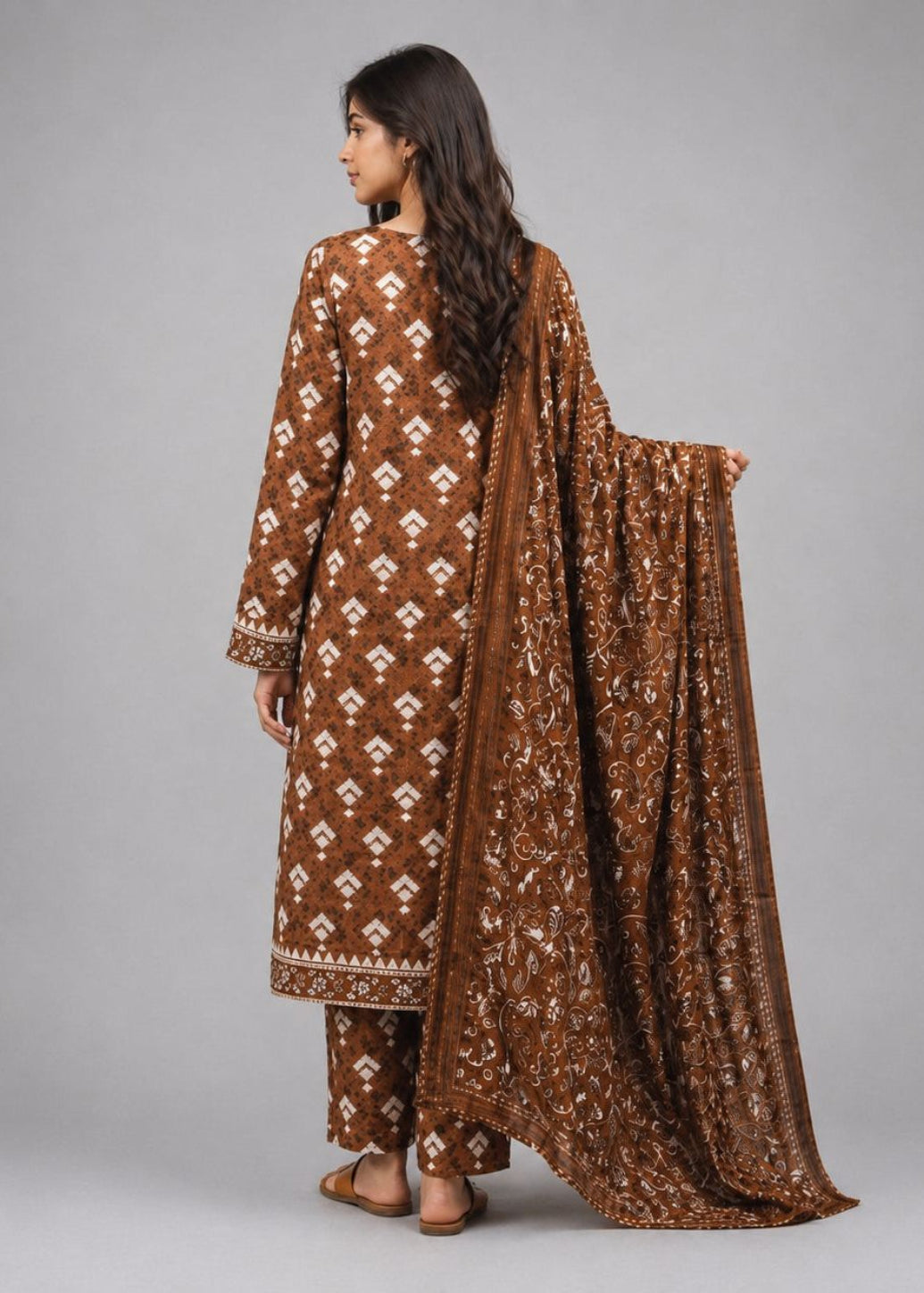 A woman modeling a brown traditional outfit with white geometric patterns, shown from the back against a solid gray studio background.