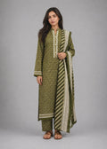 A woman modeling a three-piece olive green and beige printed ethnic suit with a matching dupatta, standing against a neutral gray studio background.