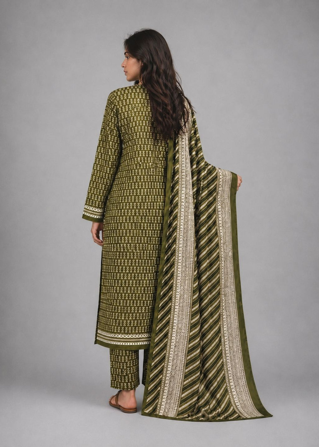A woman shown from the back wearing an olive green and beige patterned traditional outfit with matching pants and a long patterned dupatta, photographed against a plain gray studio background.