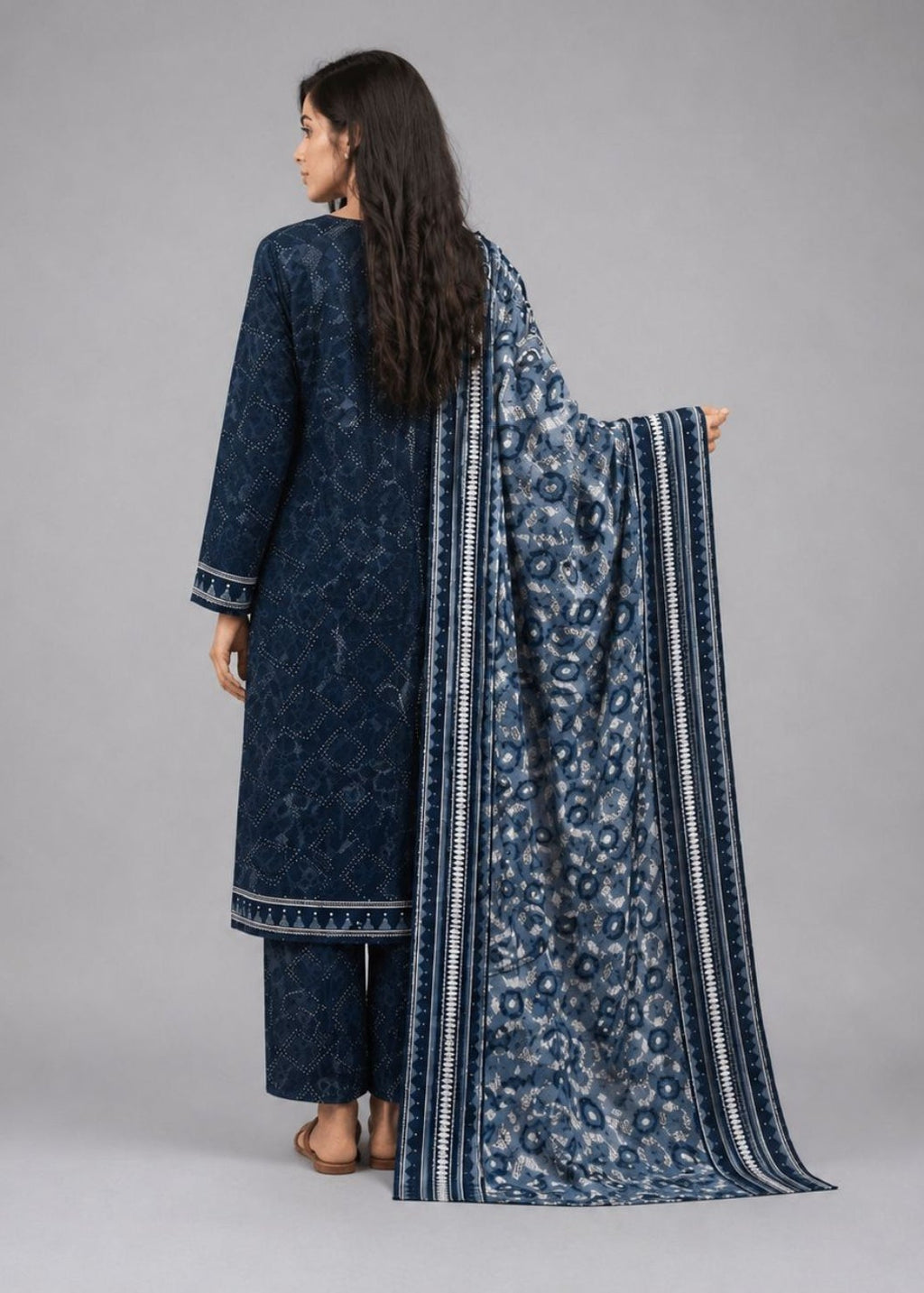 A woman shown from the back wearing a dark blue patterned traditional outfit with matching pants and a draped dupatta, photographed against a plain light gray studio background.