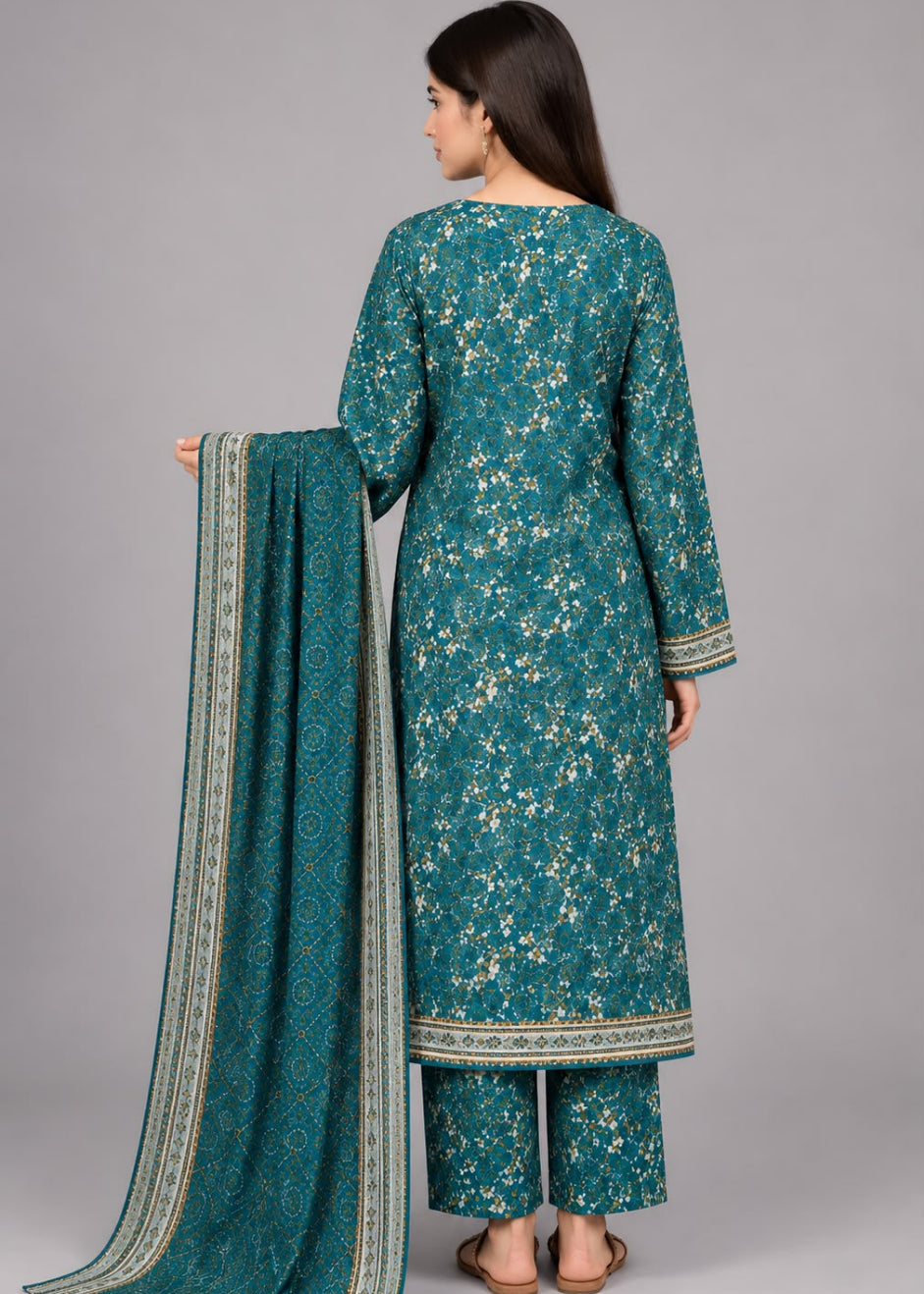 A woman shown from the back wearing a teal three-piece salwar kameez suit with beige floral prints and holding a matching dupatta with a beige border, against a solid gray studio background.