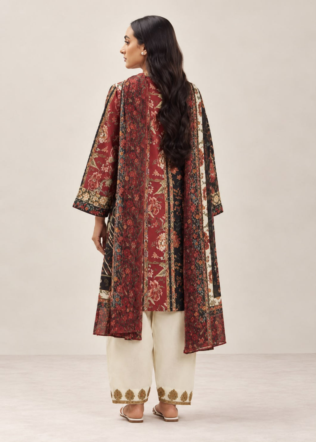 A woman shown from the back wearing a long red printed kurta with beige and gold patterns, paired with cream-colored pants, against a neutral studio background.