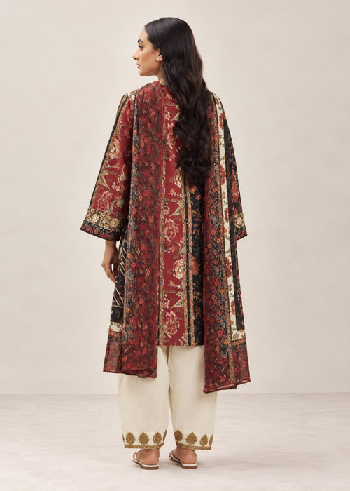 A woman shown from the back wearing a long red printed kurta with beige and gold patterns, paired with cream-colored pants, against a neutral studio background.