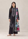 A woman modeling a black three-piece traditional outfit with intricate silver embroidery on the kurta, black wide-leg trousers, and a colorful floral printed dupatta, set against a plain beige studio background.