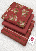 A stack of folded red fabric pieces, likely bed sheets or a bedding set, featuring a green and beige leaf pattern and a decorative border. A white tag with a red horse logo and the text 'Bin Saeed' is attached.